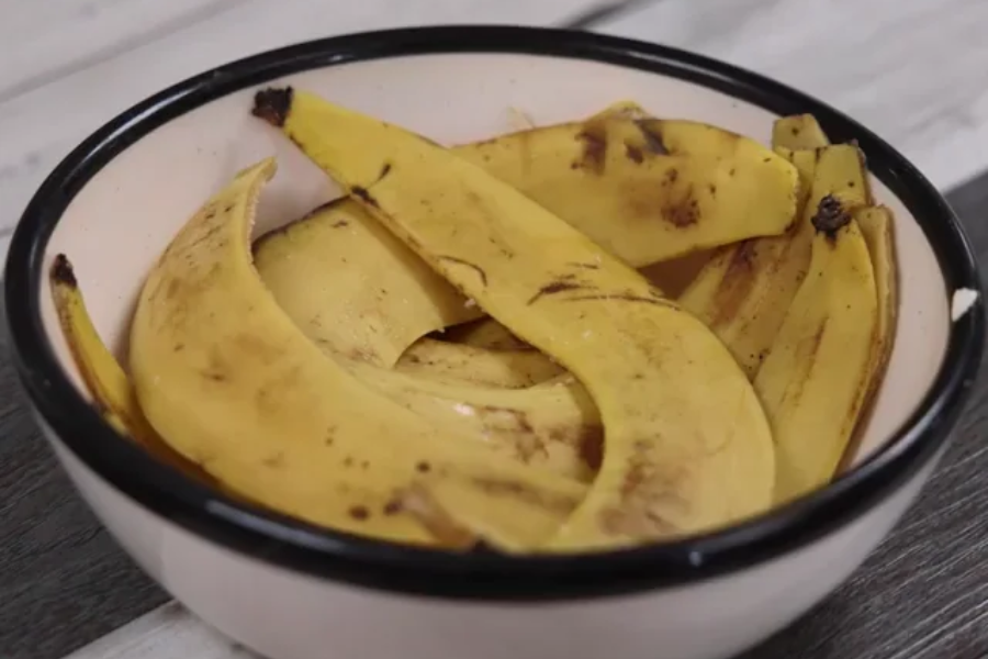 A bowl filled with several used banana peels, showing brown spots and dark bruises. The peels are arranged loosely in a white bowl with a black rim, resting on a wooden surface.