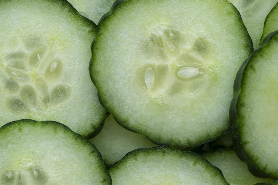 Close-up view of fresh cucumber slices, showcasing their crisp, pale green flesh and dark green skin edges. The seeds and moist texture are clearly visible, emphasizing their freshness.
