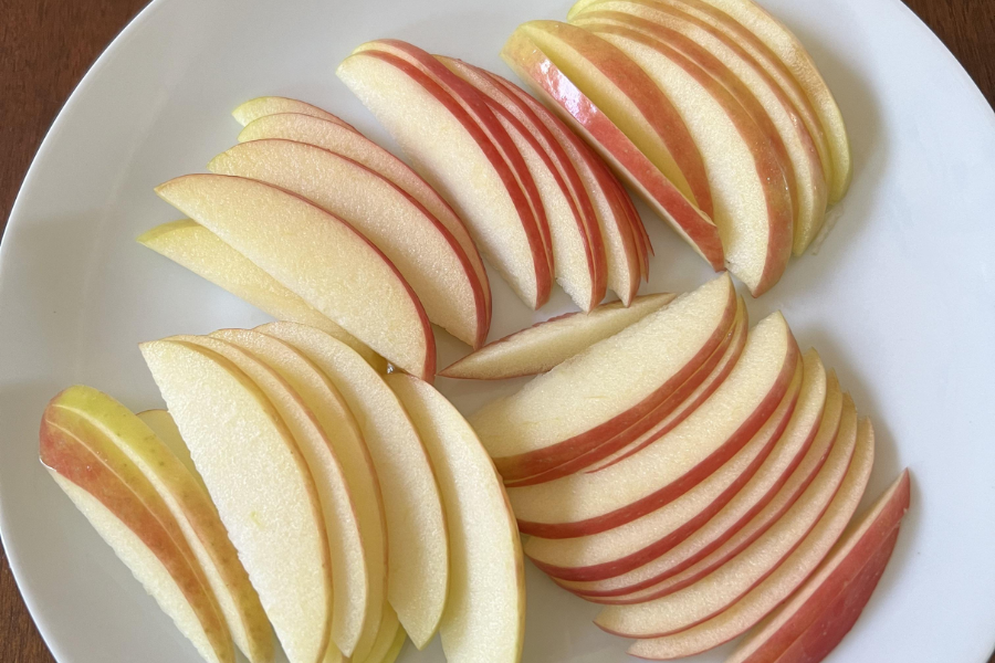 A white plate neatly arranged with thinly sliced red apples, fanned out in small overlapping sections. The apple slices have a crisp texture and glossy skin, with the white flesh contrasting the red edges.