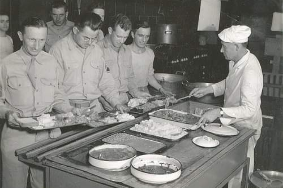 ww2 soldiers standing in a cafeteria line being served food