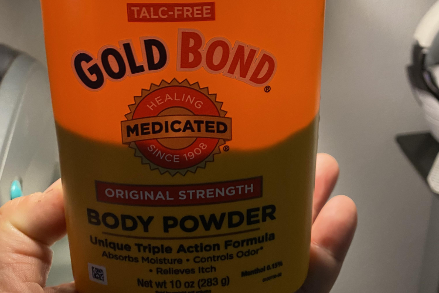 A hand holding a container of Gold Bond Medicated Body Powder, labeled “Talc-Free” and “Original Strength,” with claims to absorb moisture, control odor, and relieve itch.