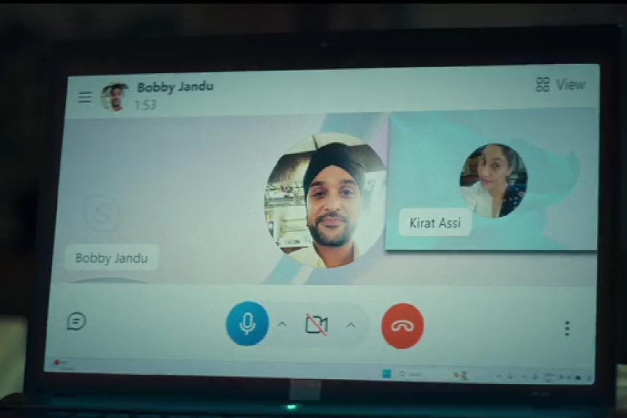 A laptop screen displays a video call between Bobby Jandu and Kirat Assi, with profile pictures visible for both. The call interface shows the camera muted, microphone on, and the red end call button.