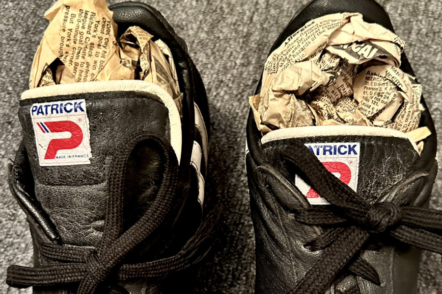 A pair of black leather Patrick sneakers with the tongues labeled "Made in France," each shoe stuffed with crumpled newspaper to help maintain shape or absorb moisture. The shoes are placed on a gray carpeted floor.