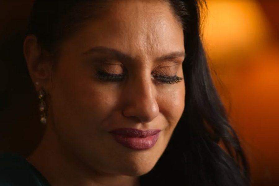 A close-up of a woman with her eyes closed and a faint, emotional expression, possibly on the verge of tears. The lighting is warm and soft, highlighting her facial features and delicate earrings.