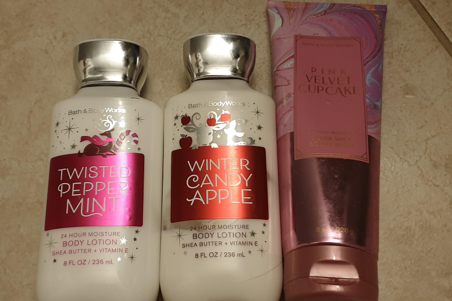 Three Bath & Body Works body lotions on a tiled surface, including Twisted Peppermint and Winter Candy Apple in white bottles with silver caps, and Pink Velvet Cupcake in a pink and purple squeeze tube.